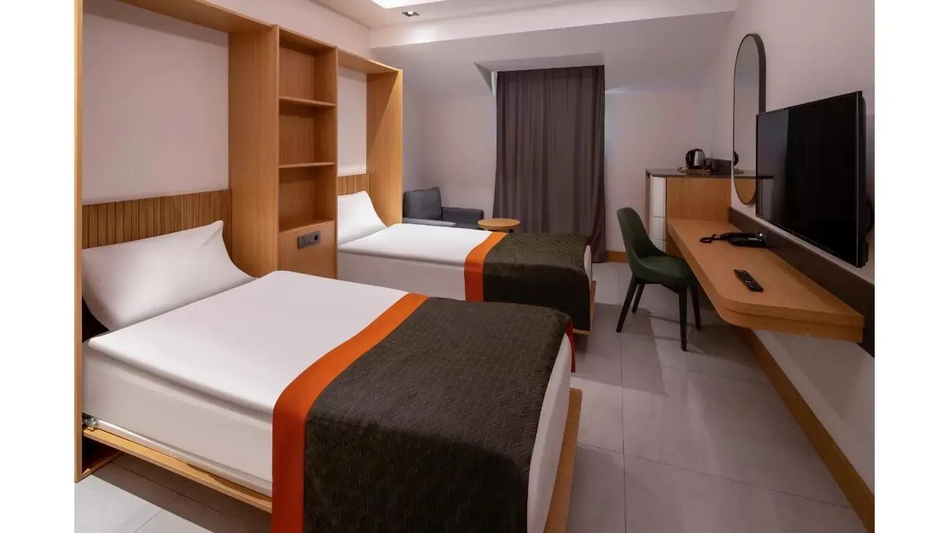 Helles Zweibettzimmer mit zwei Einzelbetten, Schreibtisch und Schrankelementen.