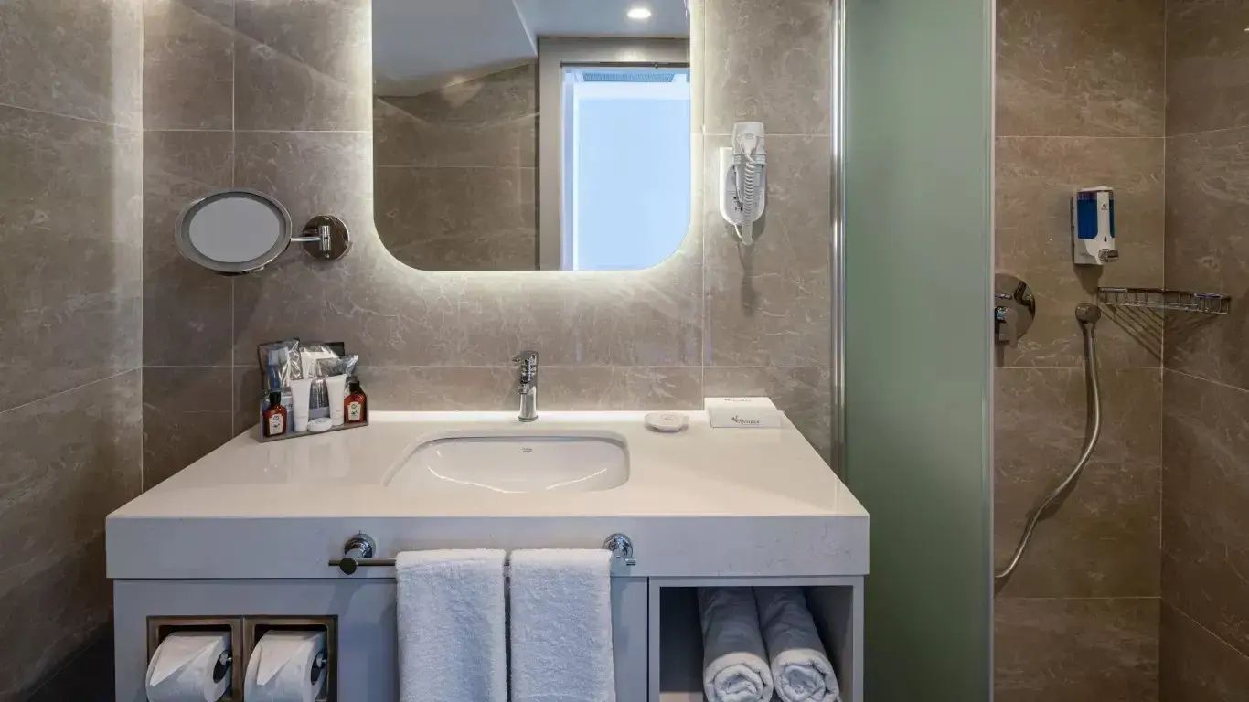 Waschtisch im Badezimmer mit beleuchtetem Spiegel und Handtüchern.