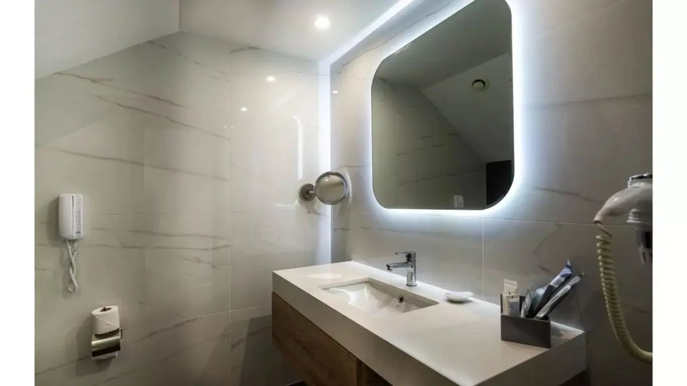 Badezimmer mit beleuchtetem Spiegel, Waschtisch aus Holz und hellen Wandfliesen.