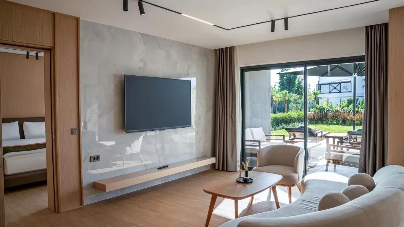 Wohnbereich einer Suite mit Fernseher an der Wand, Sessel und Terrassentür.