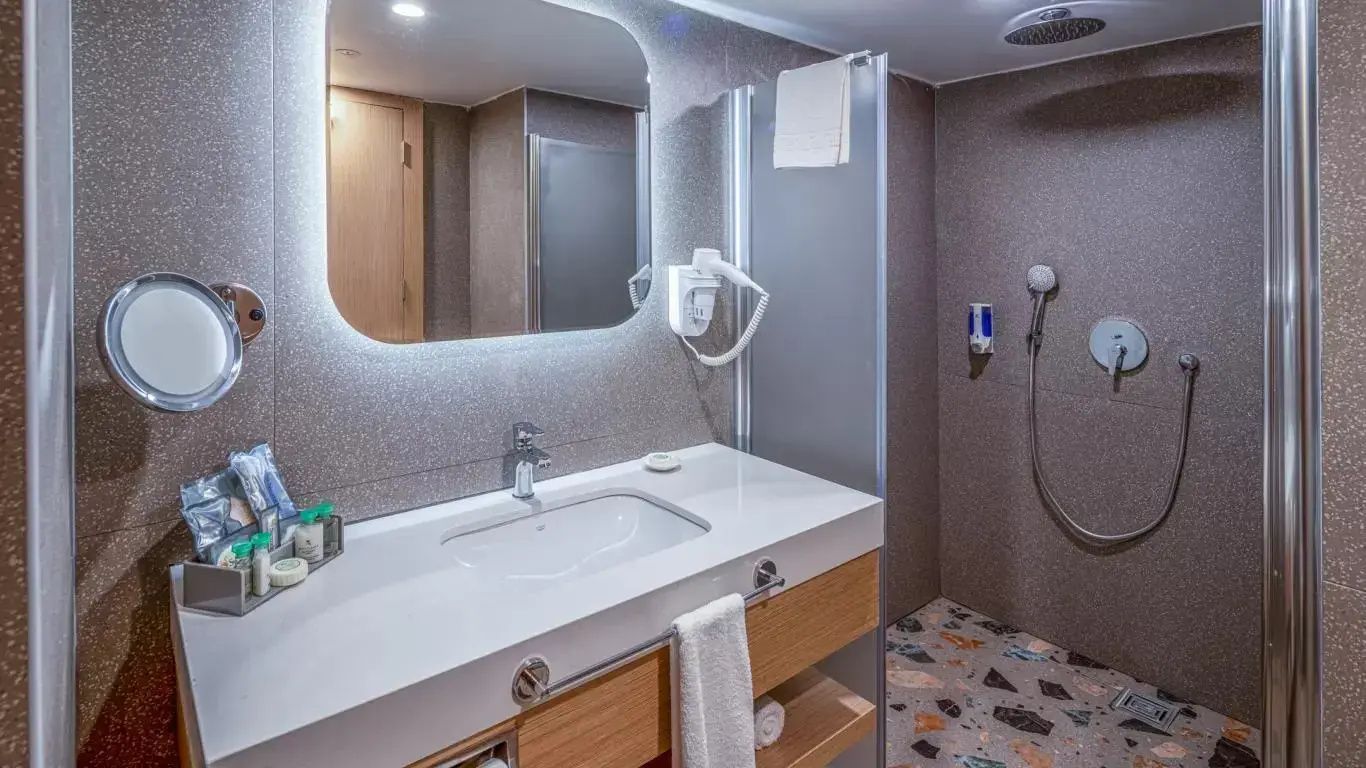 Badezimmer mit beleuchtetem Spiegel, Waschtisch und ebenerdiger Dusche.