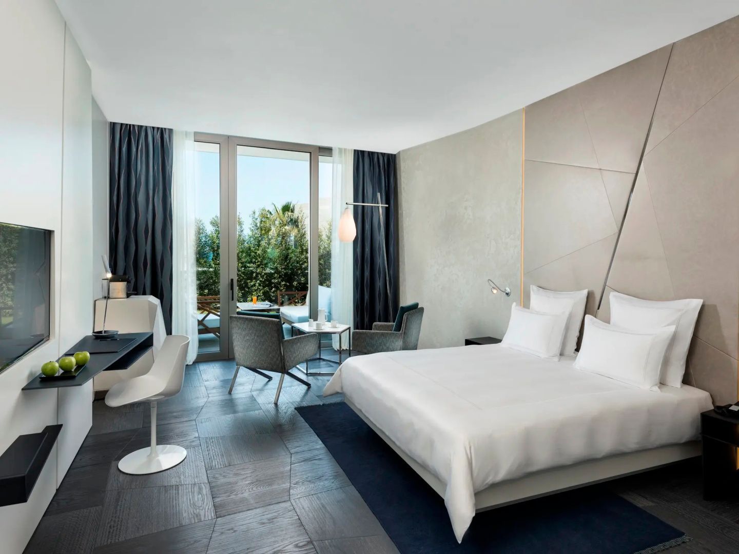 Modernes Hotelzimmer mit Doppelbett, Sitzbereich und bodentiefen Fenstern zur Terrasse.