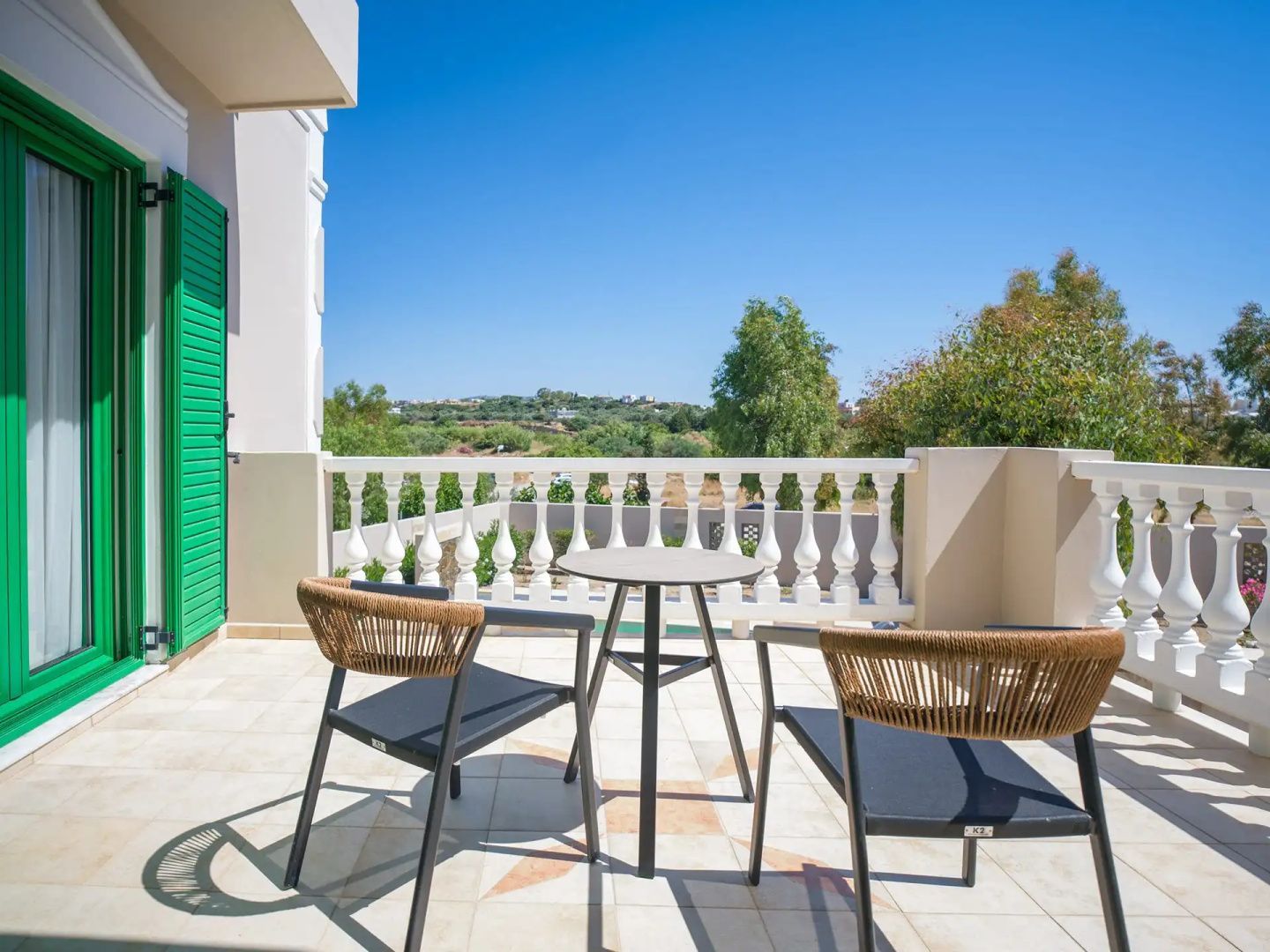 Sonnige Terrasse mit zwei Stühlen, einem Tisch und Blick auf eine grüne Hügellandschaft.