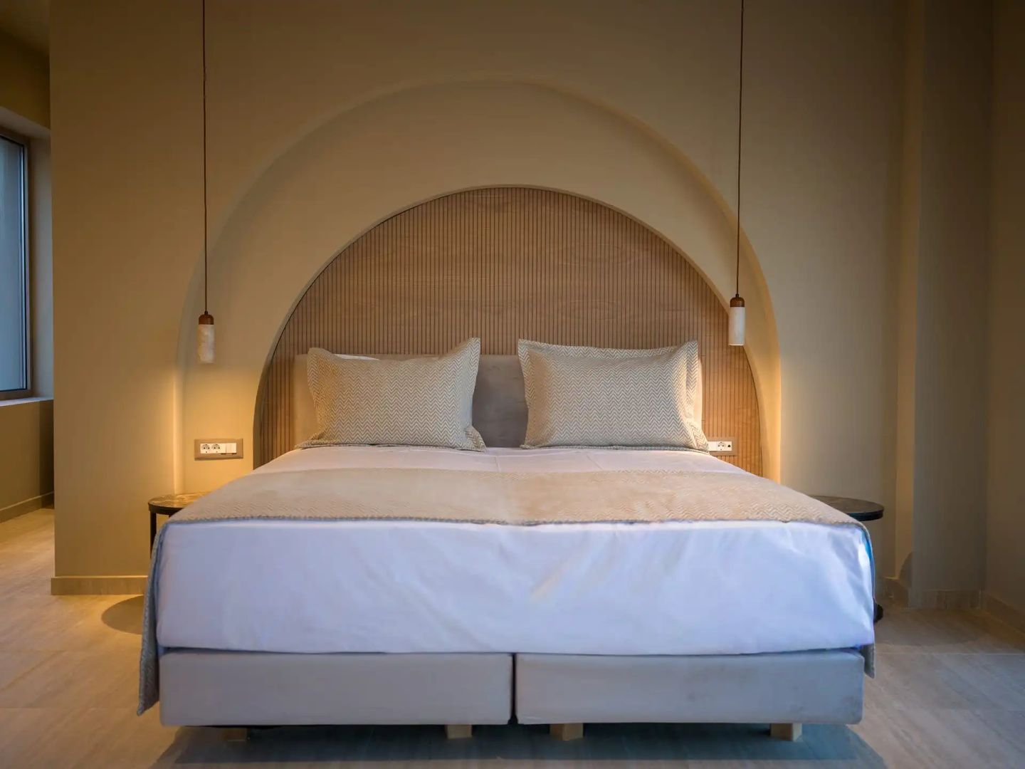 Doppelbett mit hellem Kopfteil in einer Rundbogennische und zwei Hängeleuchten an der Wand.
