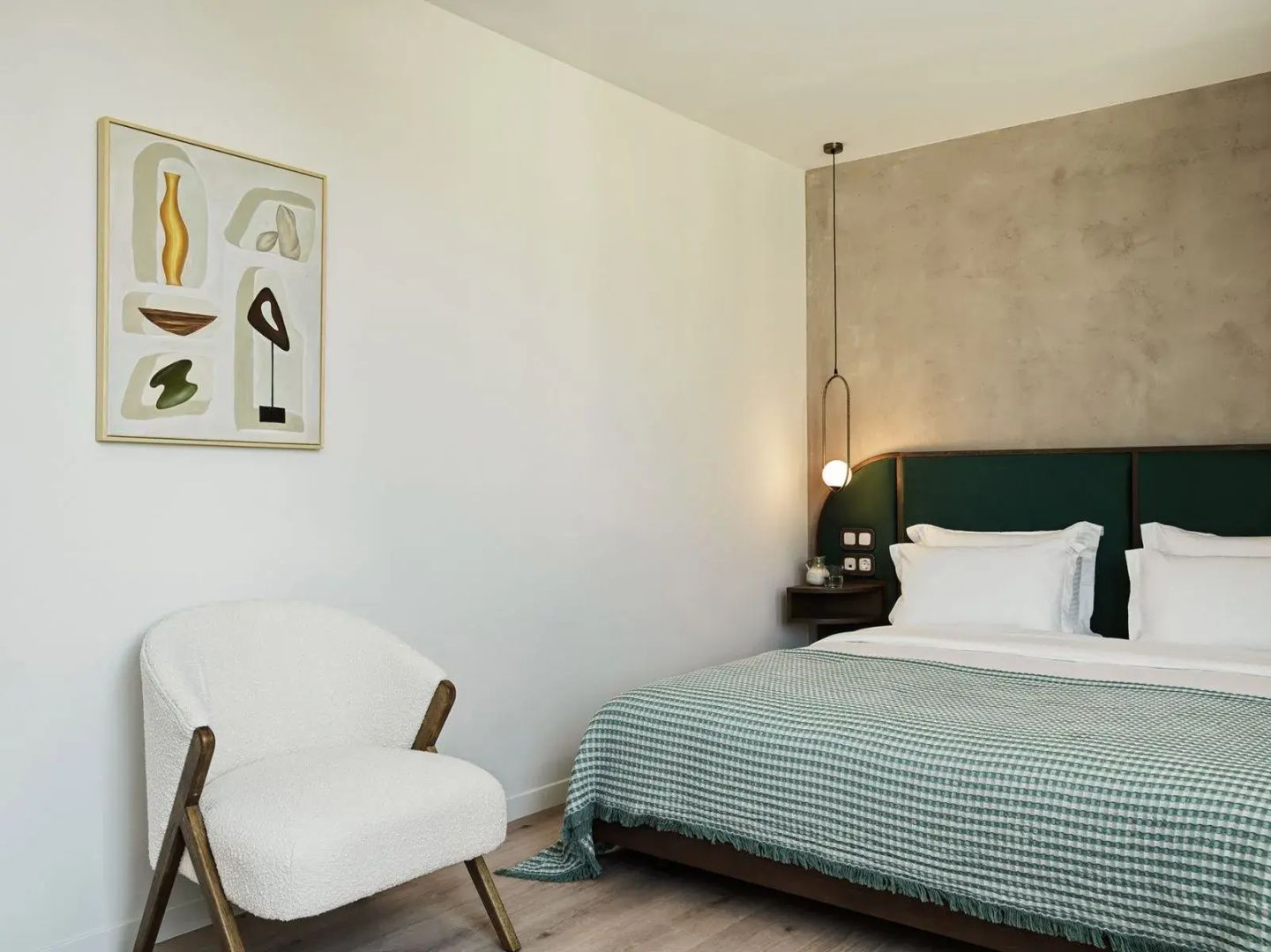 Modern eingerichtetes Hotelzimmer mit Doppelbett, grünem Kopfteil und weißem Sessel.