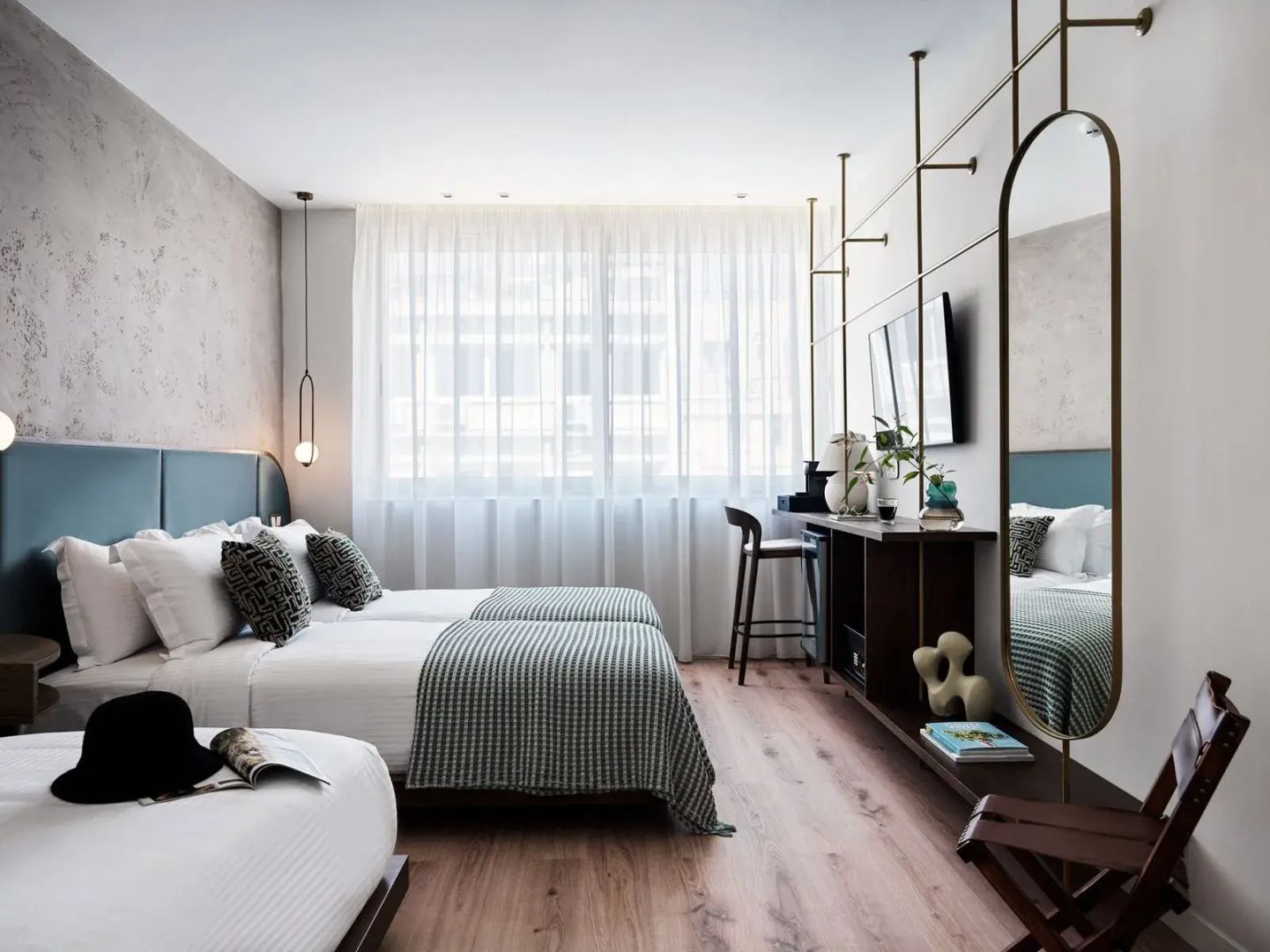 Modernes Hotelzimmer mit zwei Betten, Parkettboden und hellem Fenstervorhang.