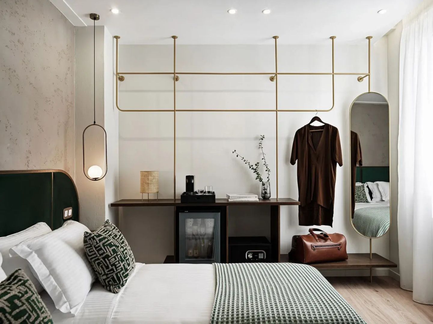 Hotelzimmer mit offener Garderobe aus Messing, Minibar, Zimmersafe und Doppelbett.