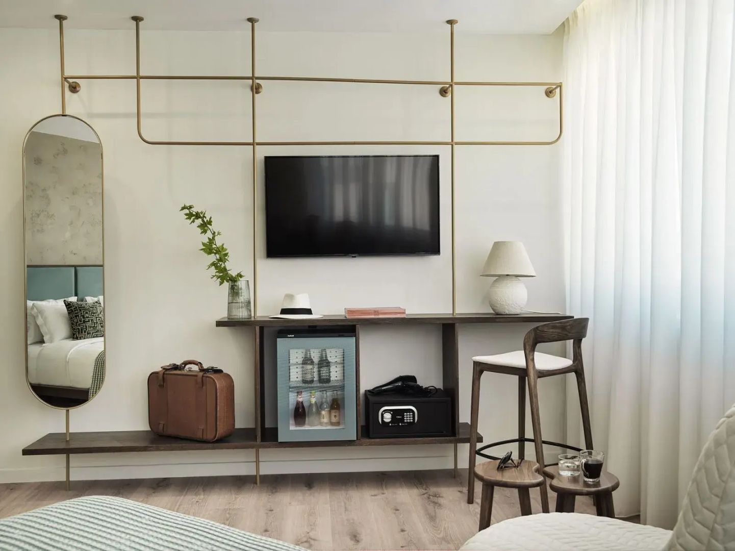 Wandregal im Hotelzimmer mit Fernseher, Minibar, Safe und einem Stuhl.