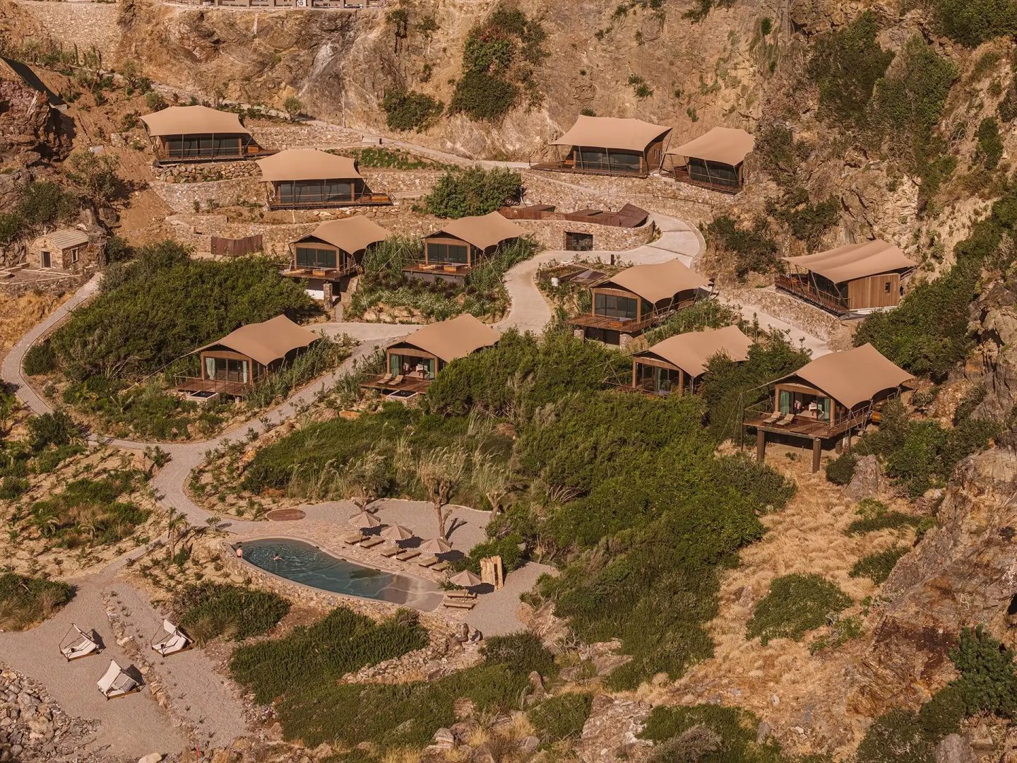 Vogelperspektive auf die in einen Hang gebettete Hotelanlage mit mehreren Bungalows.
