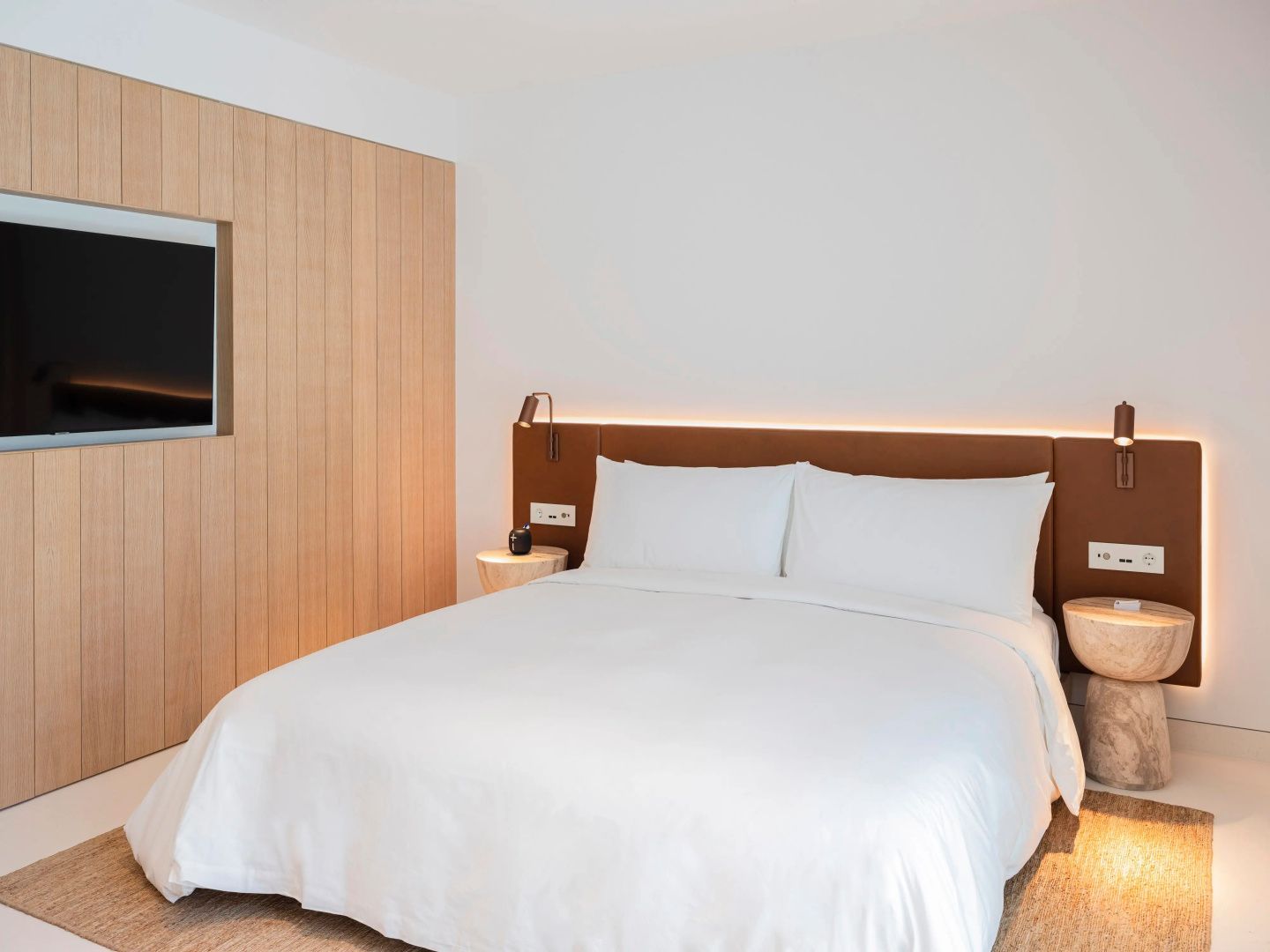 Doppelbett mit weißer Bettwäsche und braunem Kopfteil vor heller Wand im Hotelzimmer.