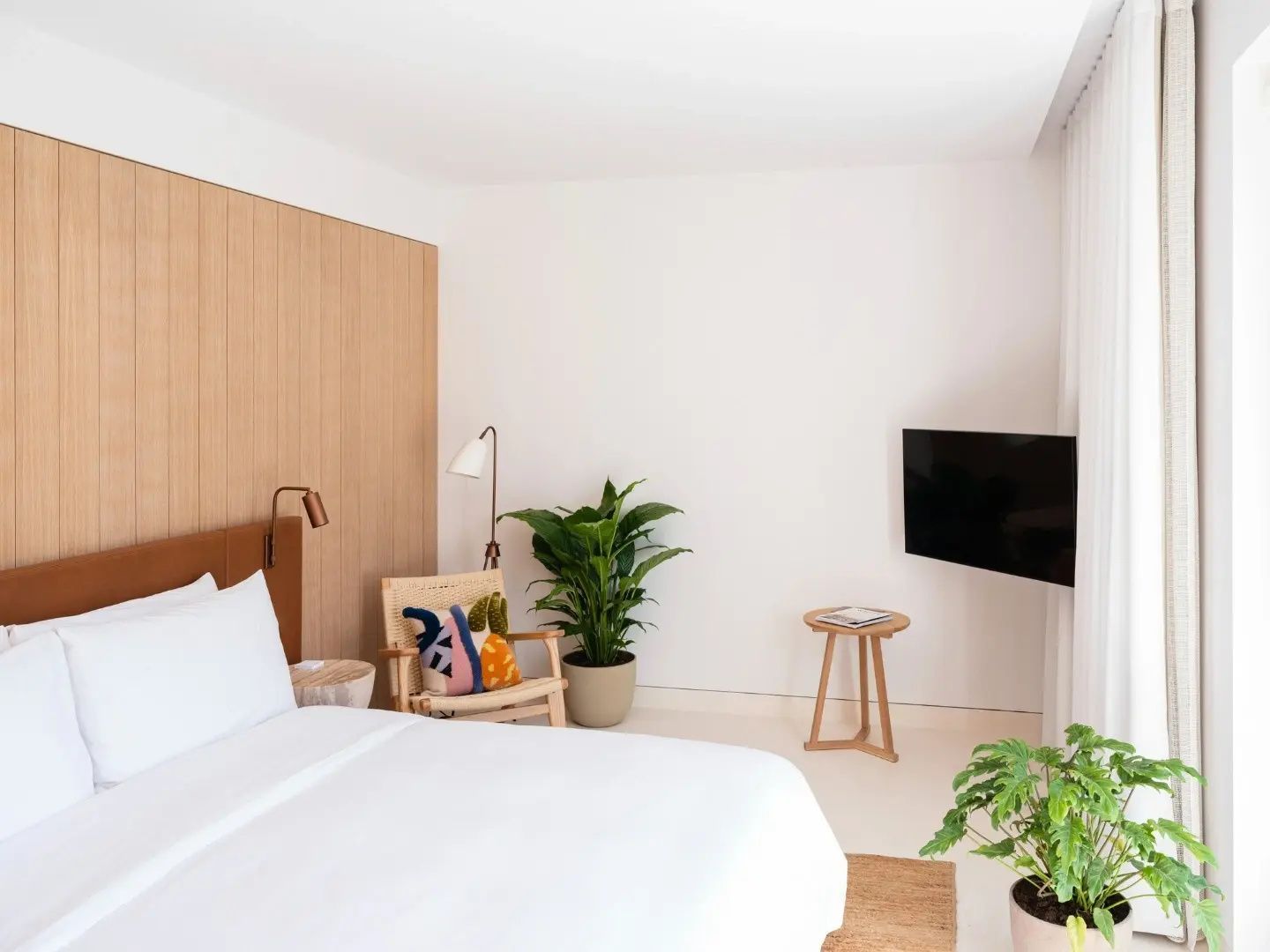 Hell eingerichtetes Hotelzimmer mit Doppelbett, Holzverkleidung, Sessel und Fernseher.