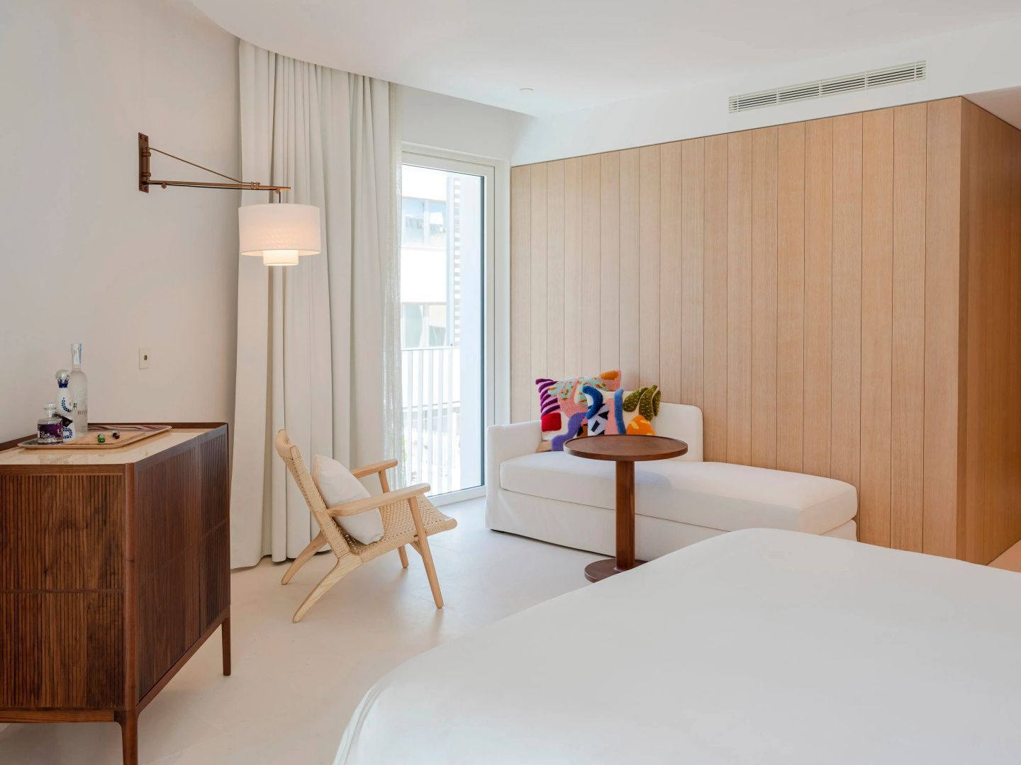 Heller Wohnbereich im Hotelzimmer mit weißem Sofa, Holzstuhl und Holzverkleidung an der Wand.