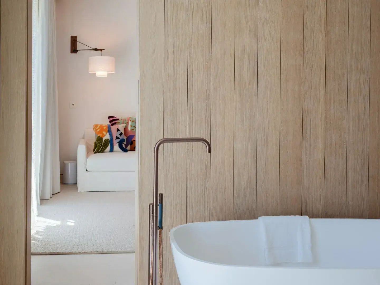 Freistehende weiße Badewanne mit moderner Armatur vor einer hellen Holzwand im Badebereich.