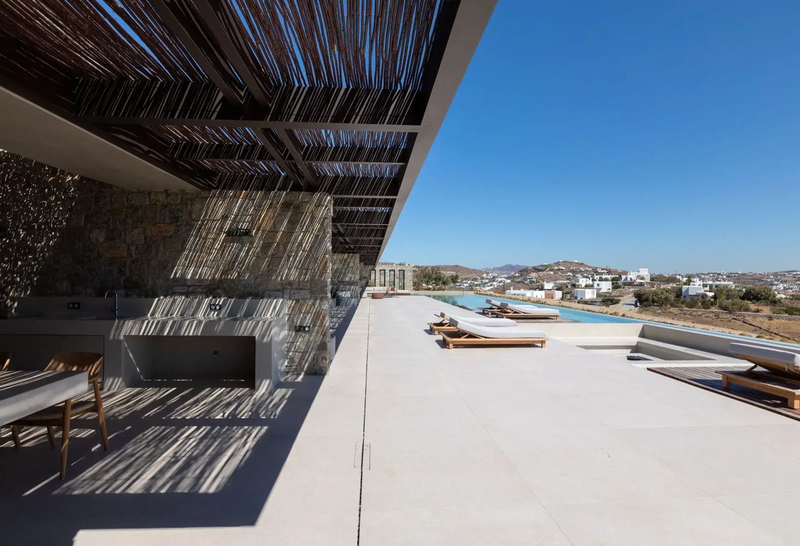 Sonnendeck mit Liegestühlen am langen Pool unter einer Holzpergola mit Blick ins Landesinnere.