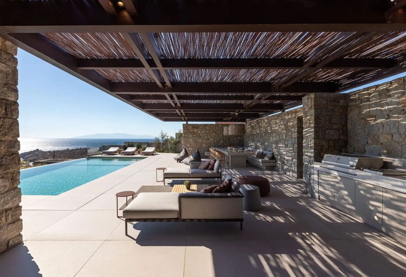 Überdachte Terrasse mit Liegestühlen und einem Pool mit Blick auf die Küstenlandschaft.