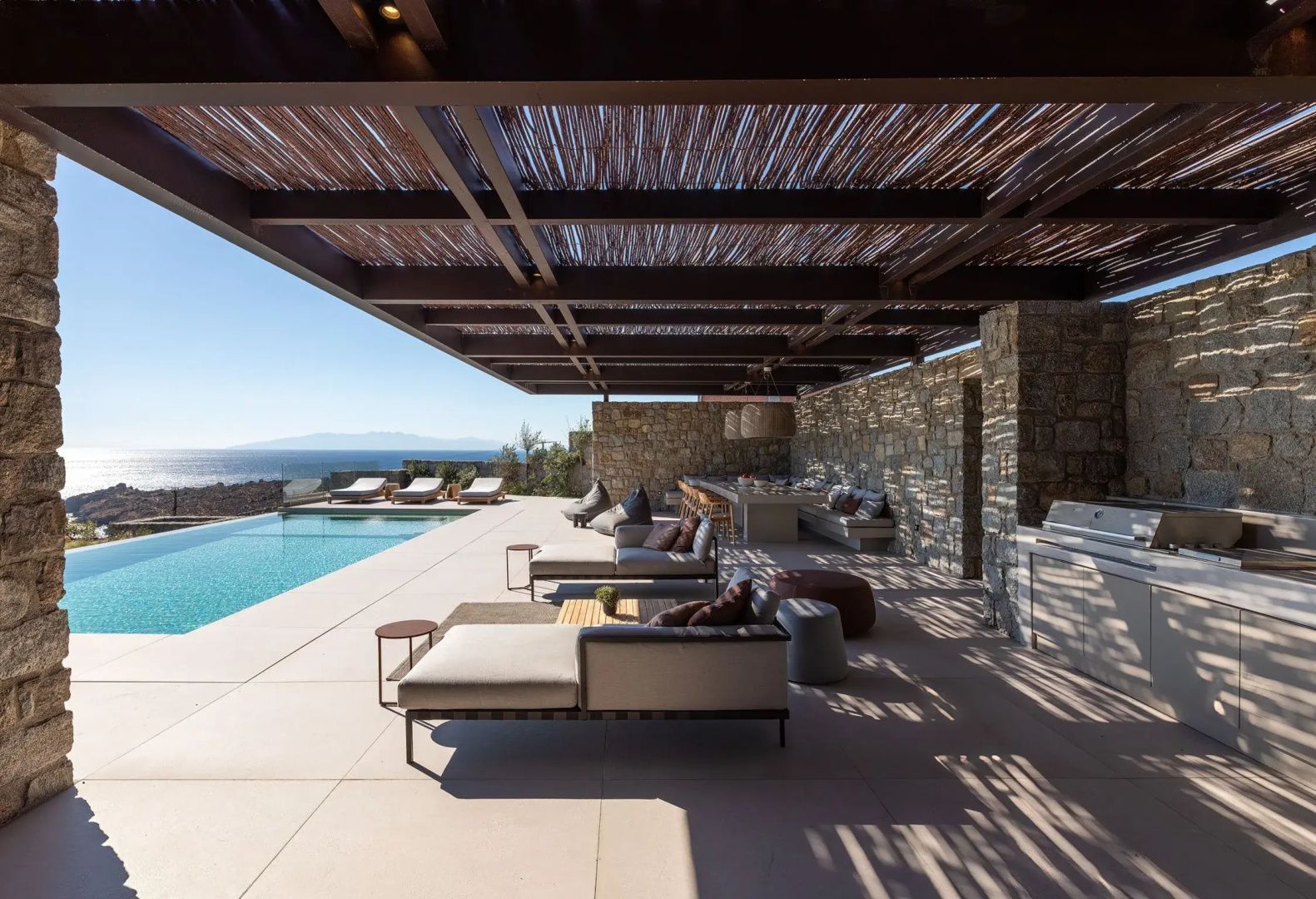 Überdachte Terrasse mit Loungemöbeln, Esstisch und Swimmingpool mit Blick auf das Meer.