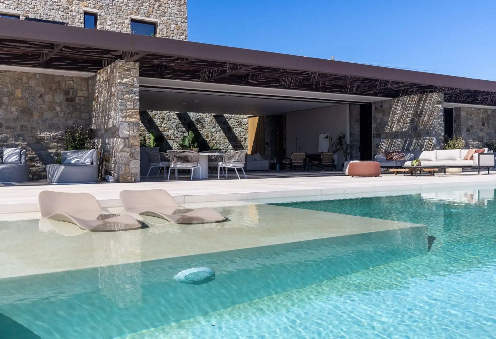 Sonnenliegen im seichten Wasser eines Swimmingpools vor einer Natursteinmauer.