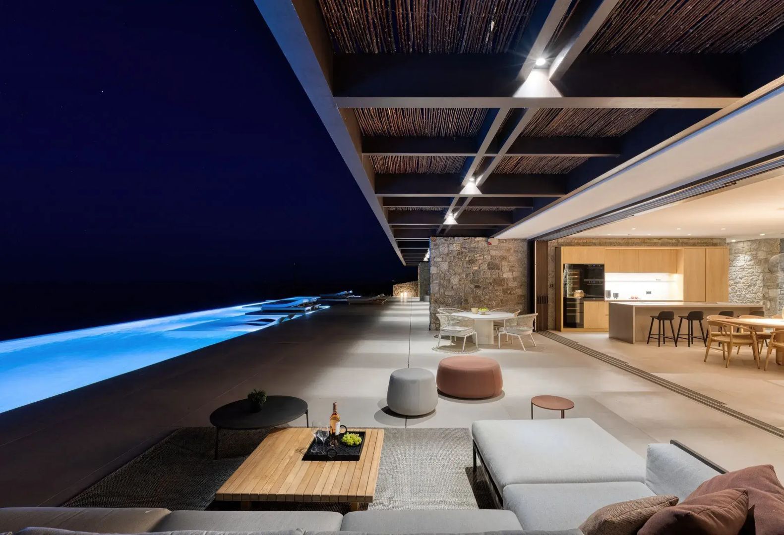 Lounge auf der Terrasse am beleuchteten Pool bei Nacht mit freiem Blick auf das Meer.