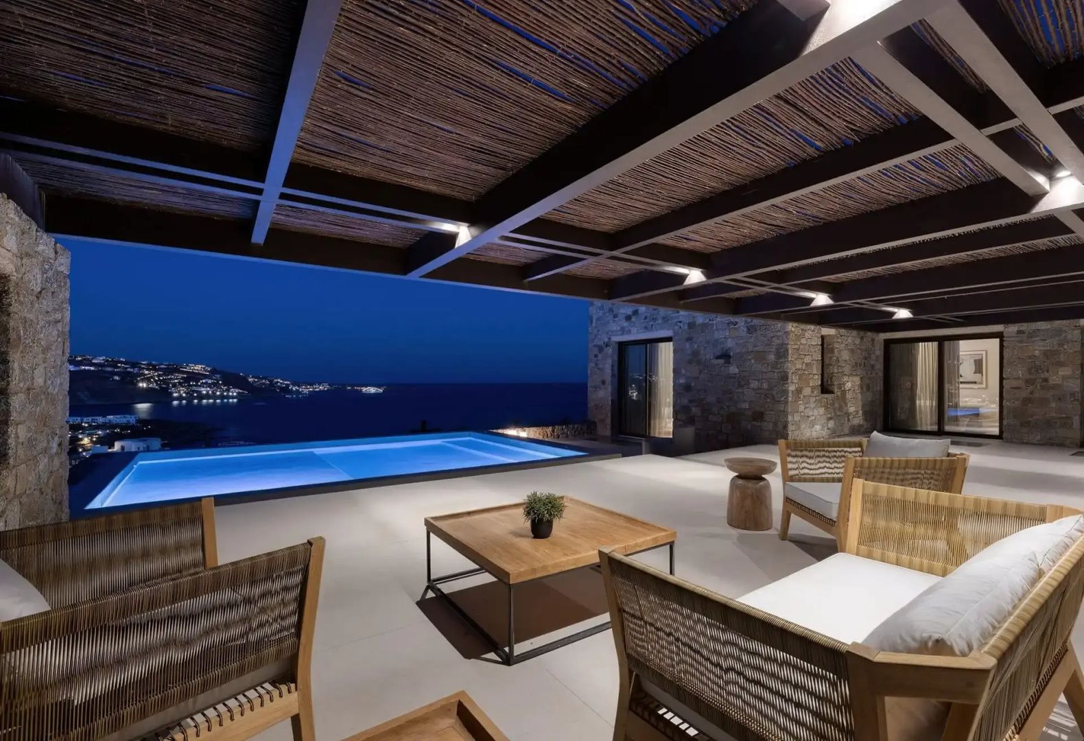 Beleuchtete Terrasse mit Holzmöbeln und Pool bei Nacht mit Blick auf das Meer.