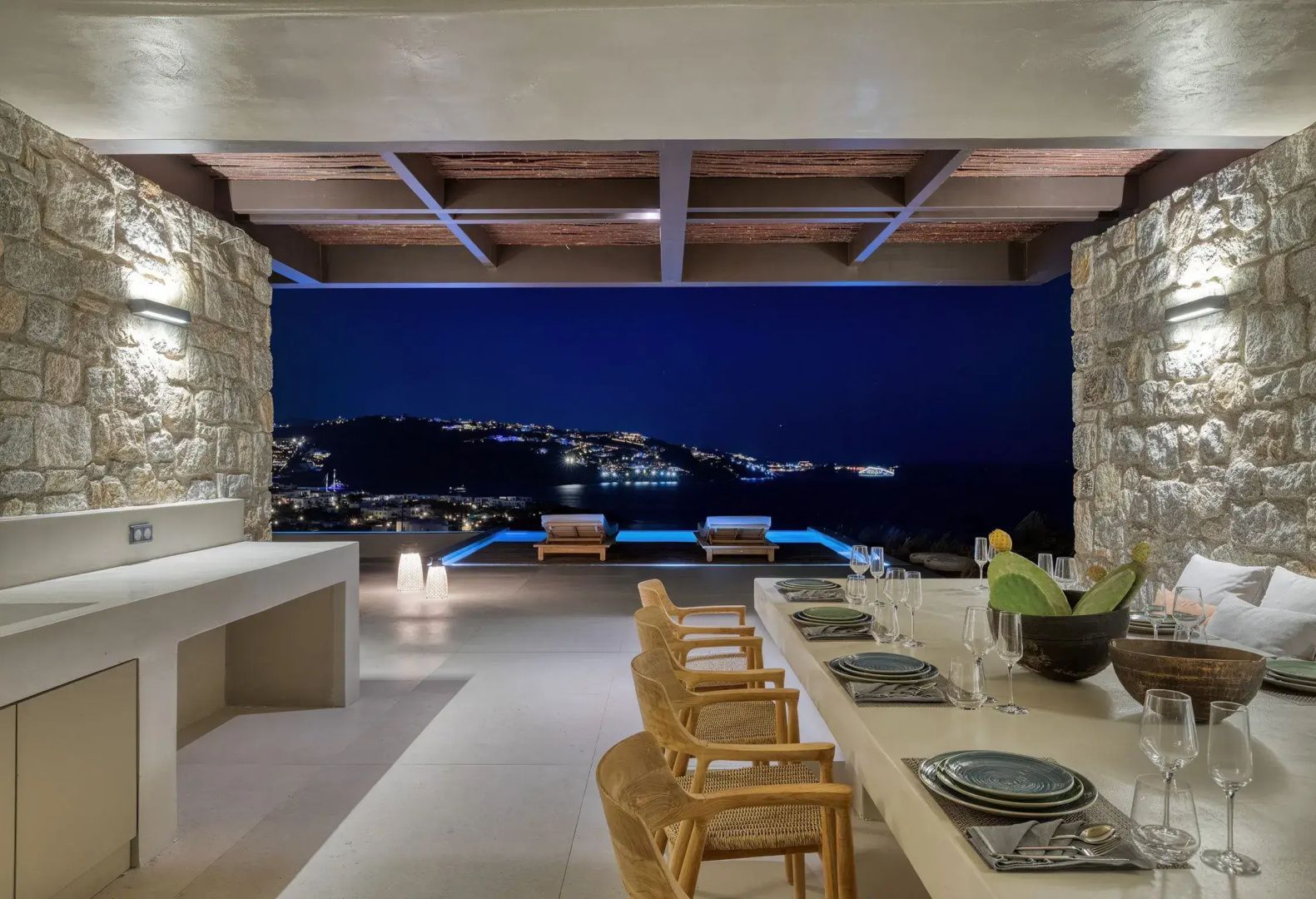 Gedeckter Esstisch auf der Terrasse mit Panoramablick auf den Pool und die Küste bei Nacht.