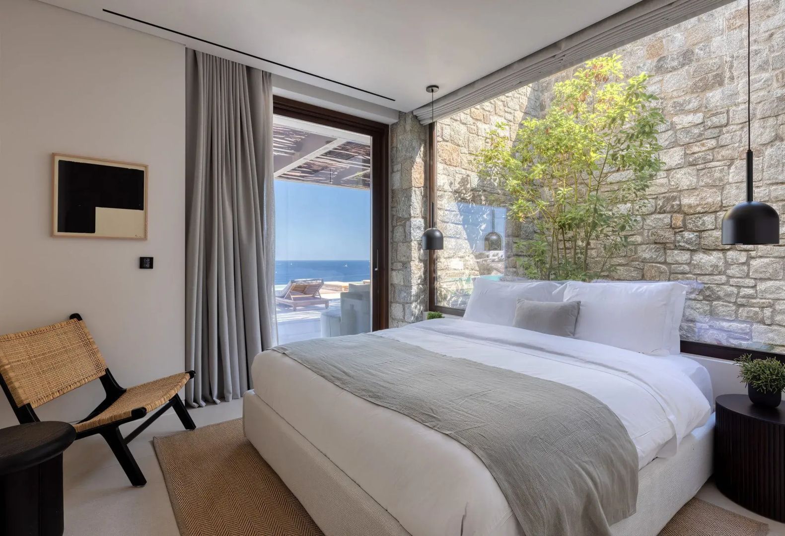 Modernes Schlafzimmer mit Doppelbett, Natursteinwand und Blick auf das Meer.
