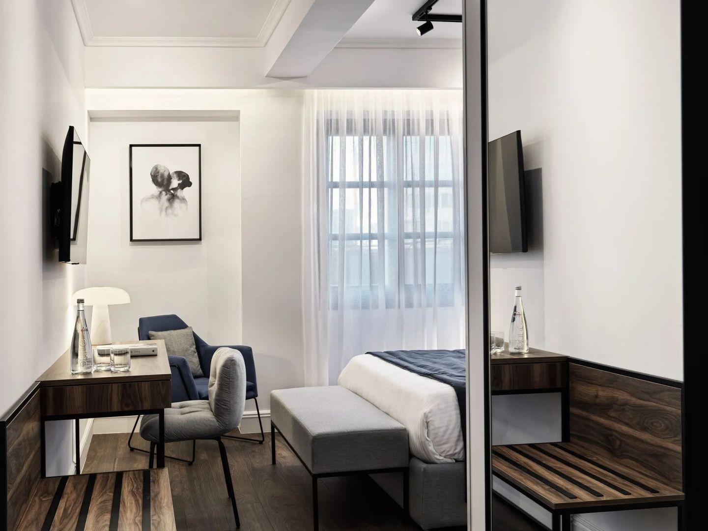 Blick in ein Hotelzimmer mit Schreibtisch, Sessel, Doppelbett und wandmontiertem Fernseher.