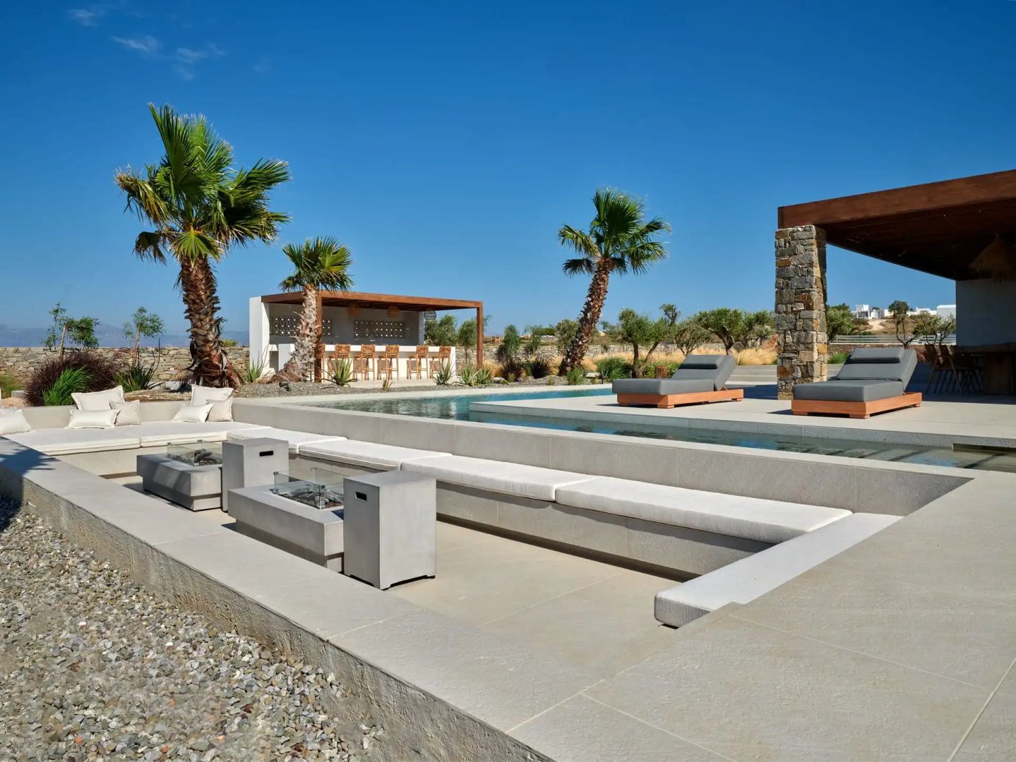 Außenbereich der Anlage mit abgesenktem Sitzbereich, Pool und Poolbar unter Palmen.