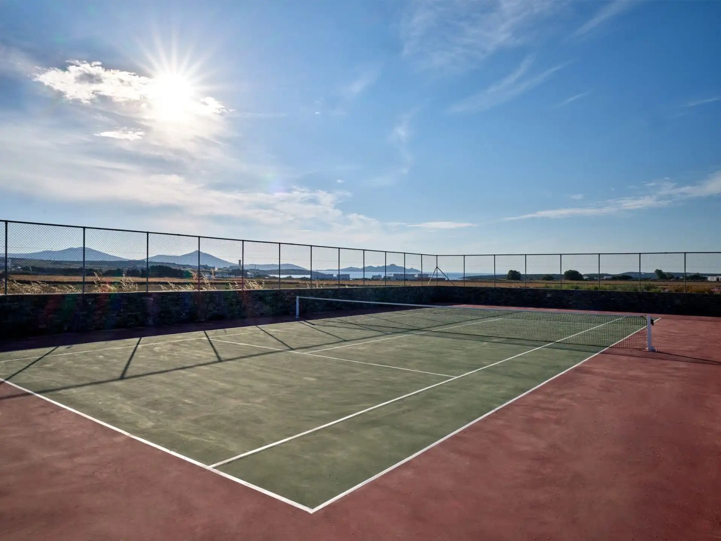 Ein Tennisplatz im Freien mit Netz und Umzäunung unter sonnigem blauen Himmel.