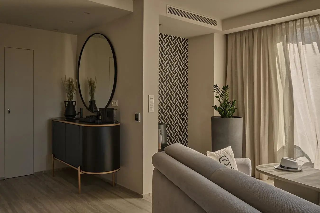 Moderne Zimmereinrichtung mit schwarzem Sideboard, ovalem Spiegel und Sofa.
