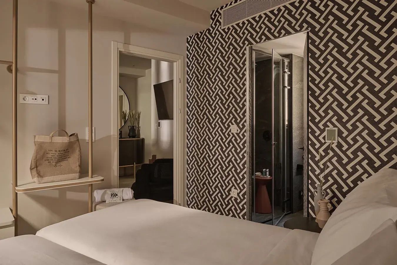 Modernes Hotelzimmer mit weiß bezogenem Bett, gemusterter Tapete und Blick ins Badezimmer.