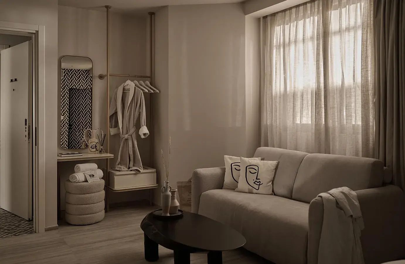 Helles Wohnzimmer mit beigem Sofa, schwarzem Couchtisch und einer offen gestalteten Garderobe.