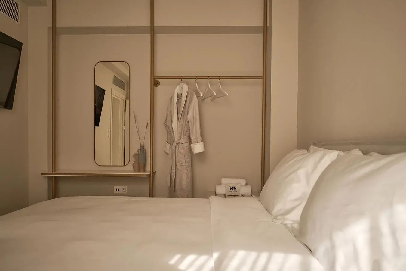 Hotelzimmer mit Doppelbett, offener Kleiderstange, Bademantel und Wandspiegel