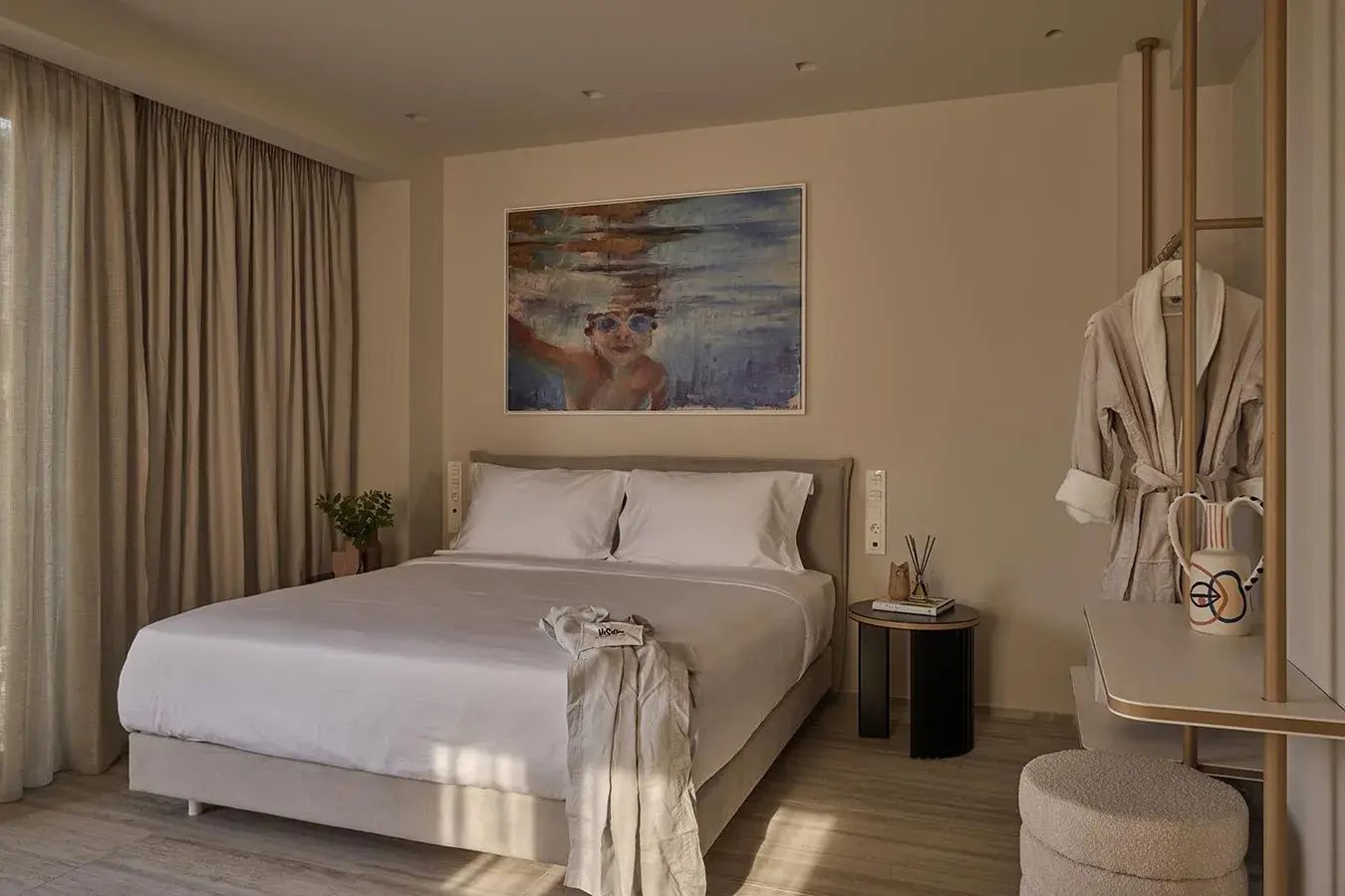Doppelbett mit weißer Bettwäsche, Wandbild darüber und Nachttisch im hellen Hotelzimmer.