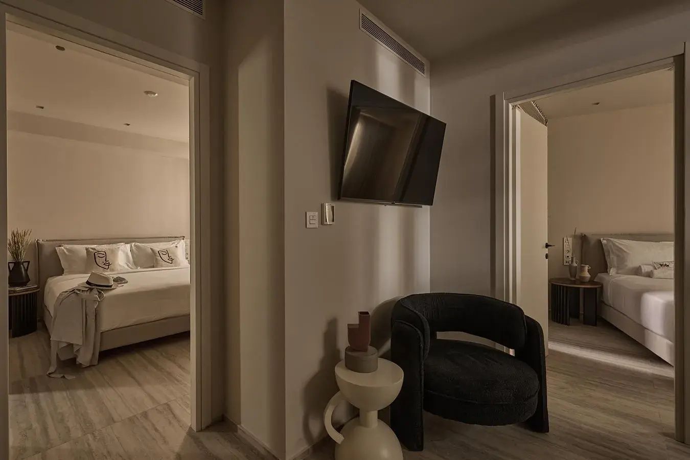 Sitzbereich mit kleinem Sessel, Wandfernseher und Blick in den Schlafbereich der Suite.