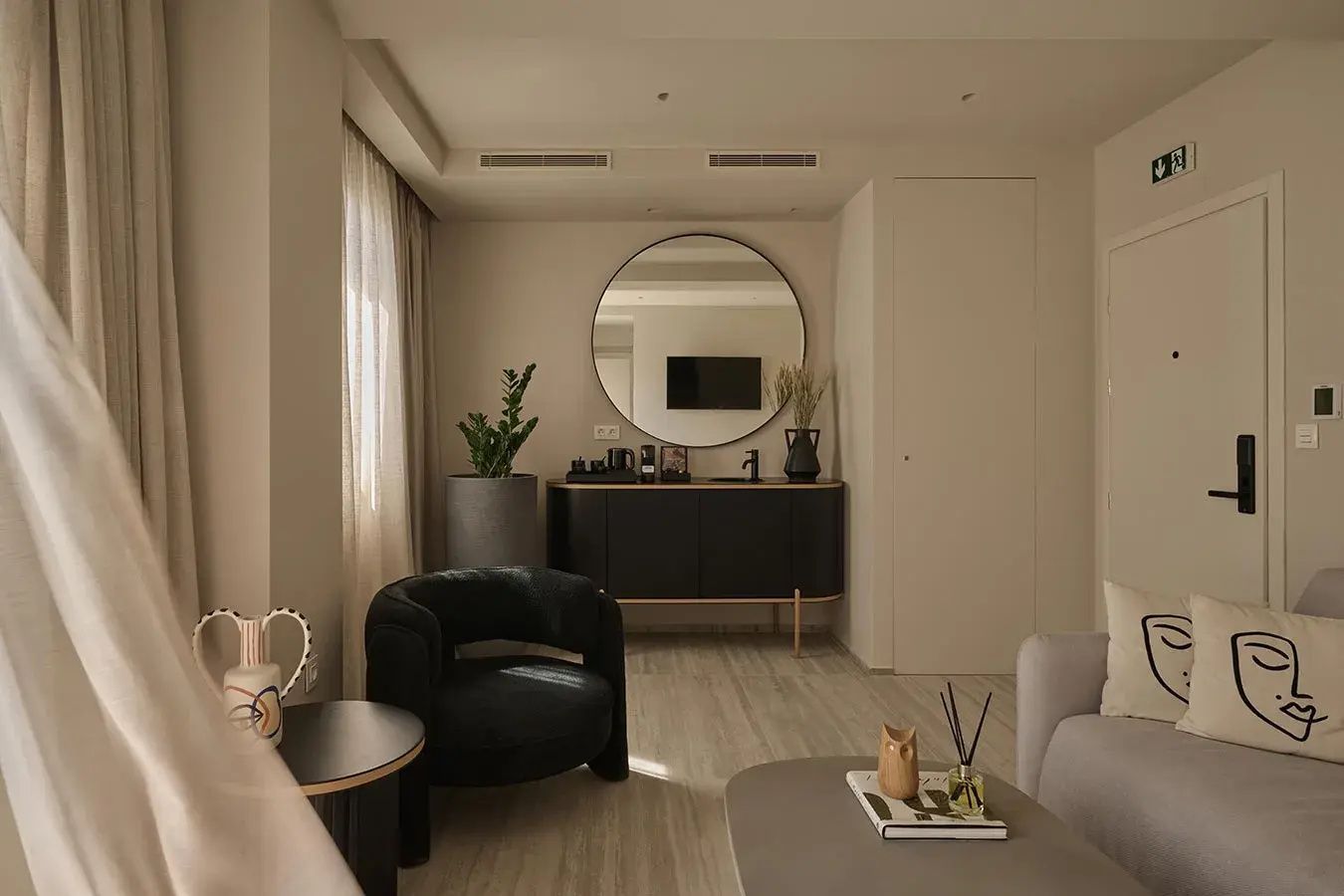 Sitzbereich im Hotelzimmer mit schwarzem Sessel, rundem Spiegel und Sideboard