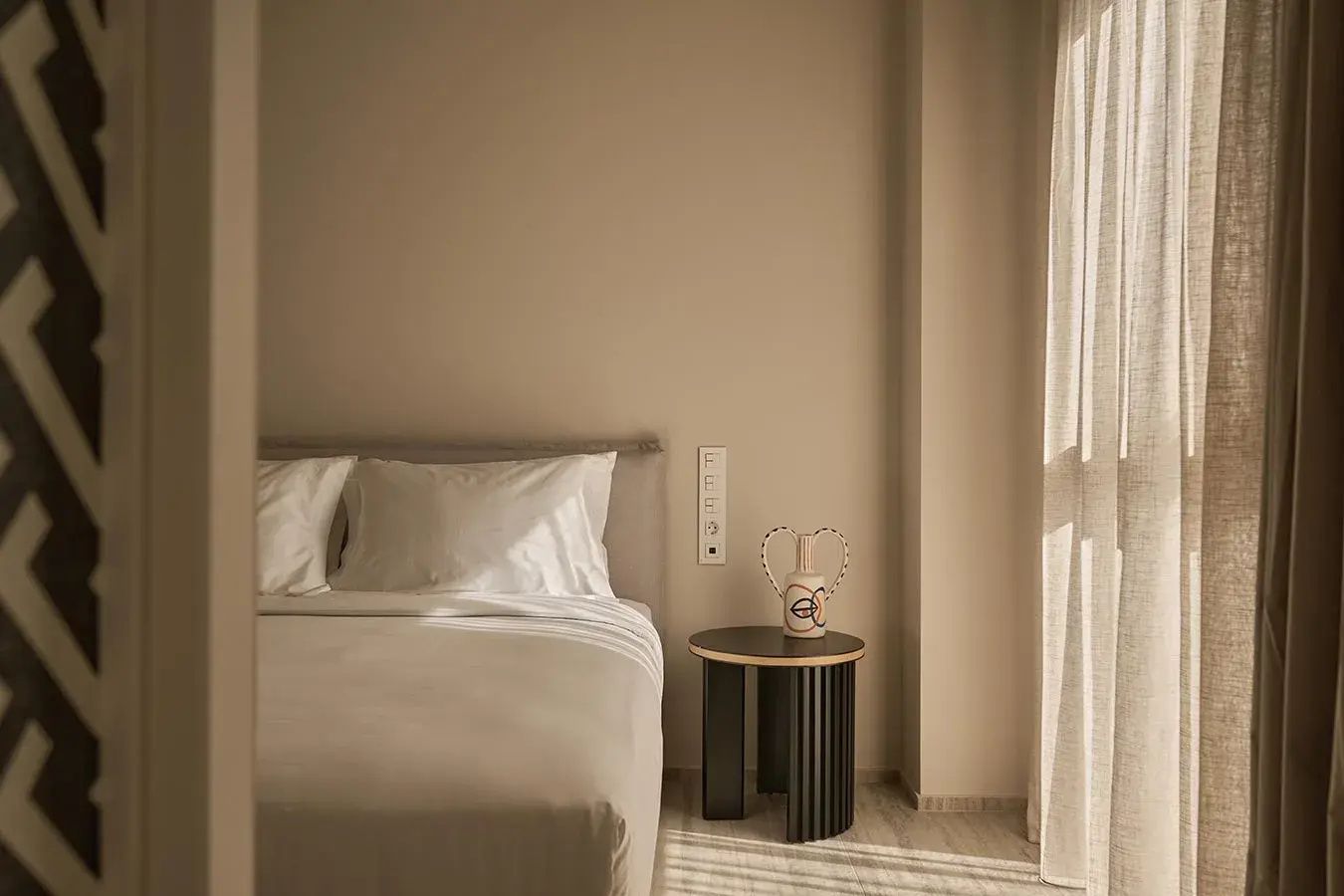 Doppelbett im Hotelzimmer mit einem kleinen Beistelltisch am Fenster