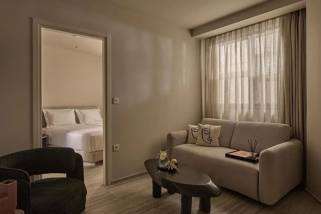 Wohnbereich einer Suite mit beigem Sofa, Couchtisch und Blick in das Schlafzimmer.