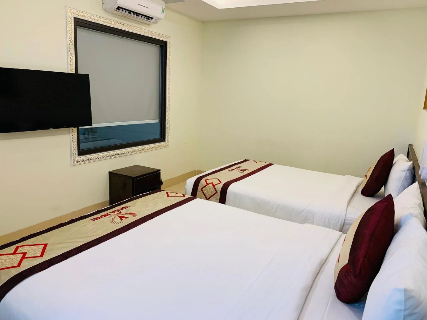 Hotelzimmer mit zwei Betten, weißer Bettwäsche, Bettläufern und einem Fernseher an der Wand.