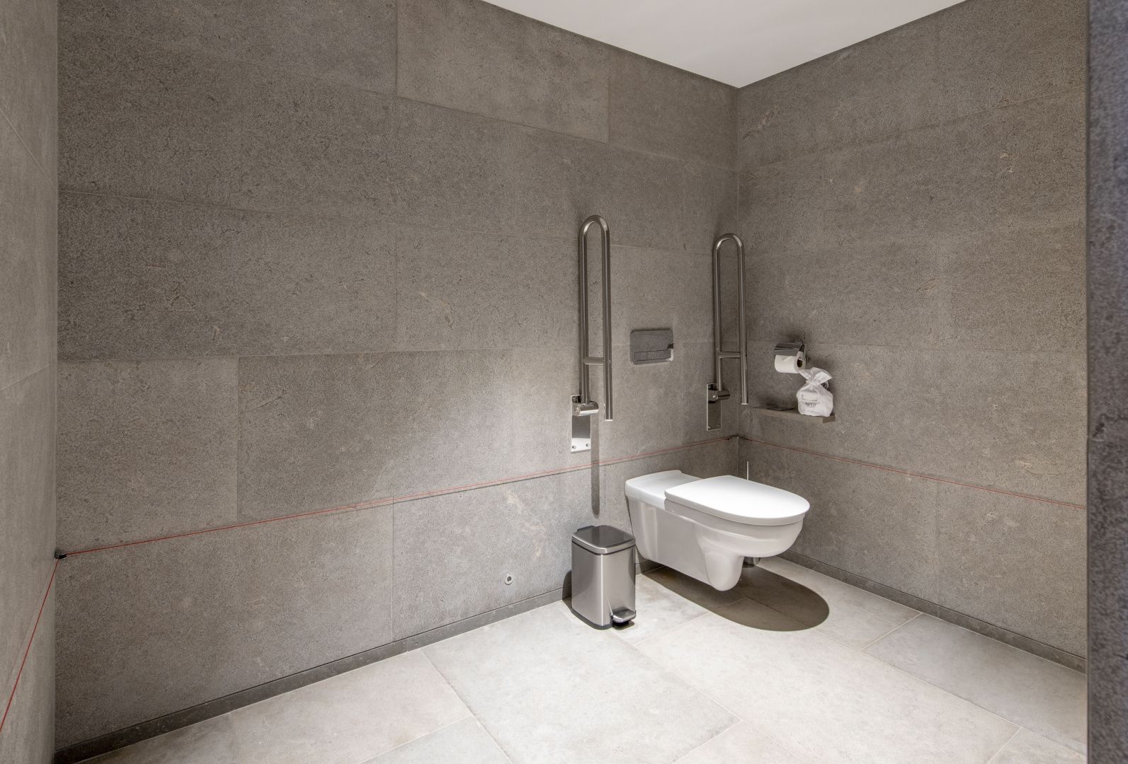 Barrierefreier Sanitärraum mit Wandtoilette und metallenen Haltegriffen.