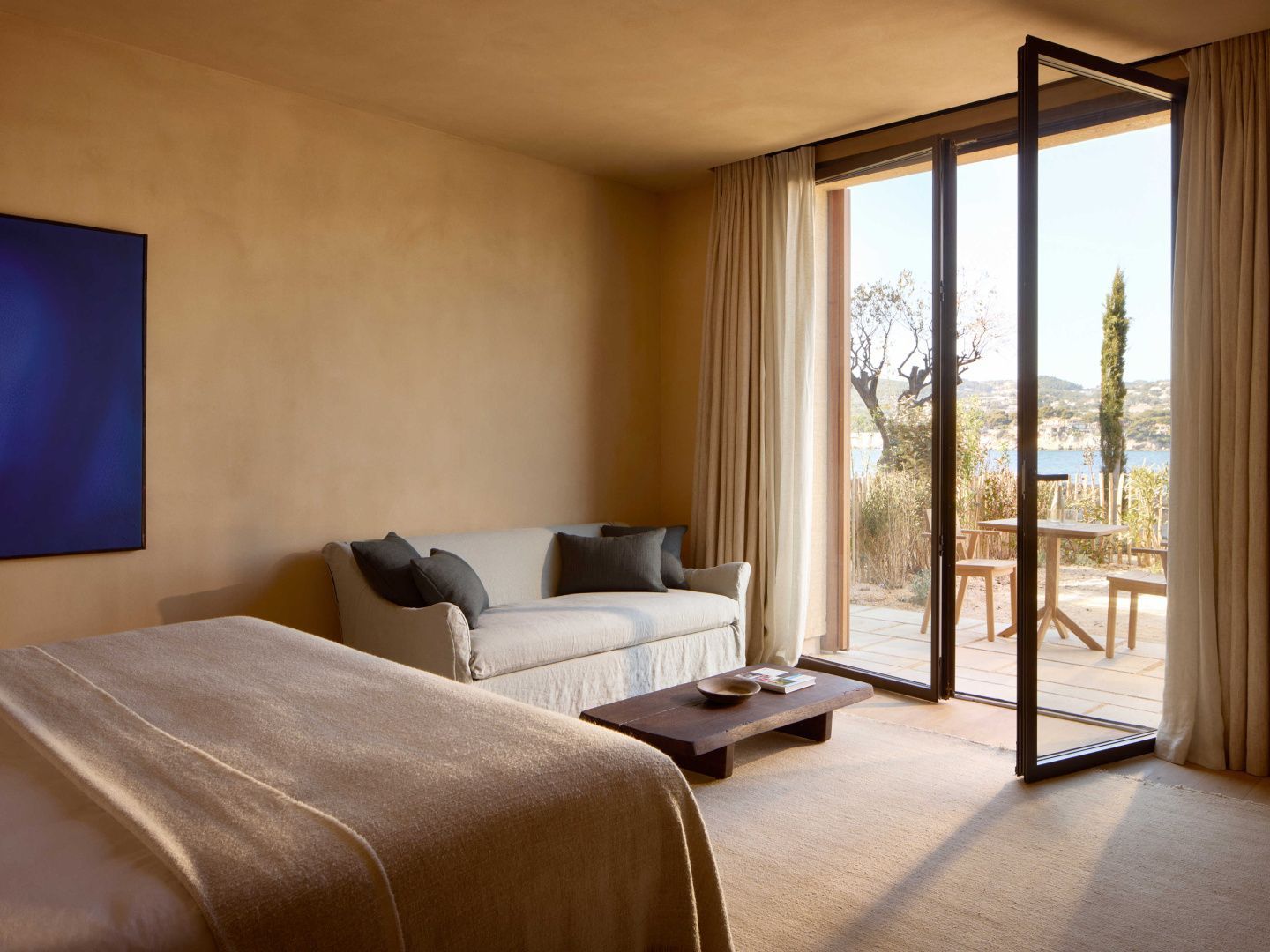 Lichtdurchflutetes Hotelzimmer mit Doppelbett, Sofa und Zugang zur sonnigen Terrasse.