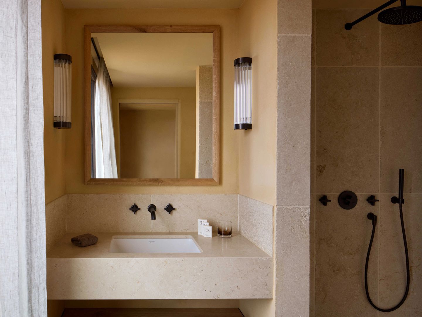 Badezimmer mit einem hellen Waschtisch, einem Holzspiegel und zwei Wandleuchten.