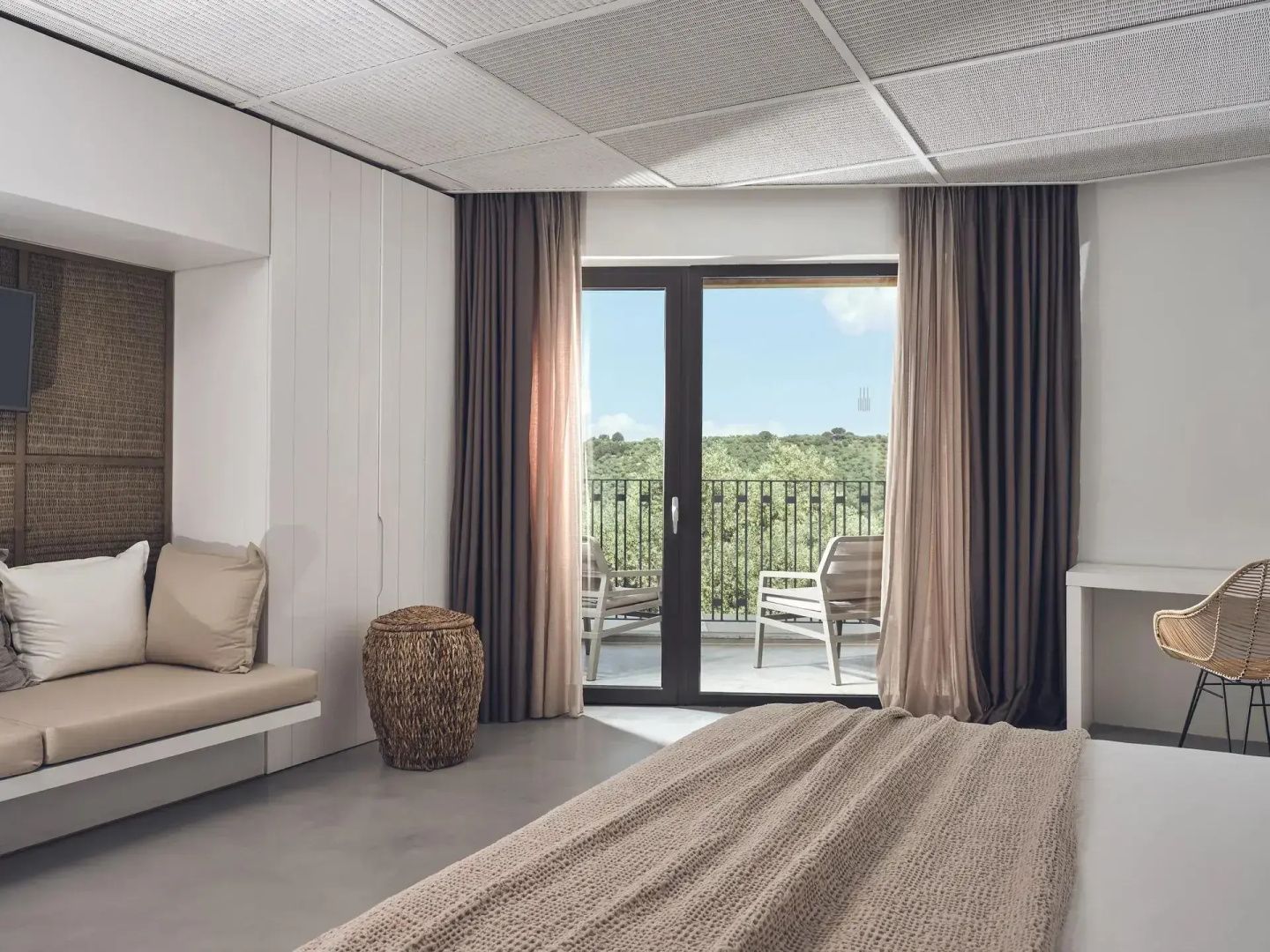 Hotelzimmer mit Blick durch die Balkontür auf zwei Stühle und grüne Bäume im Hintergrund.