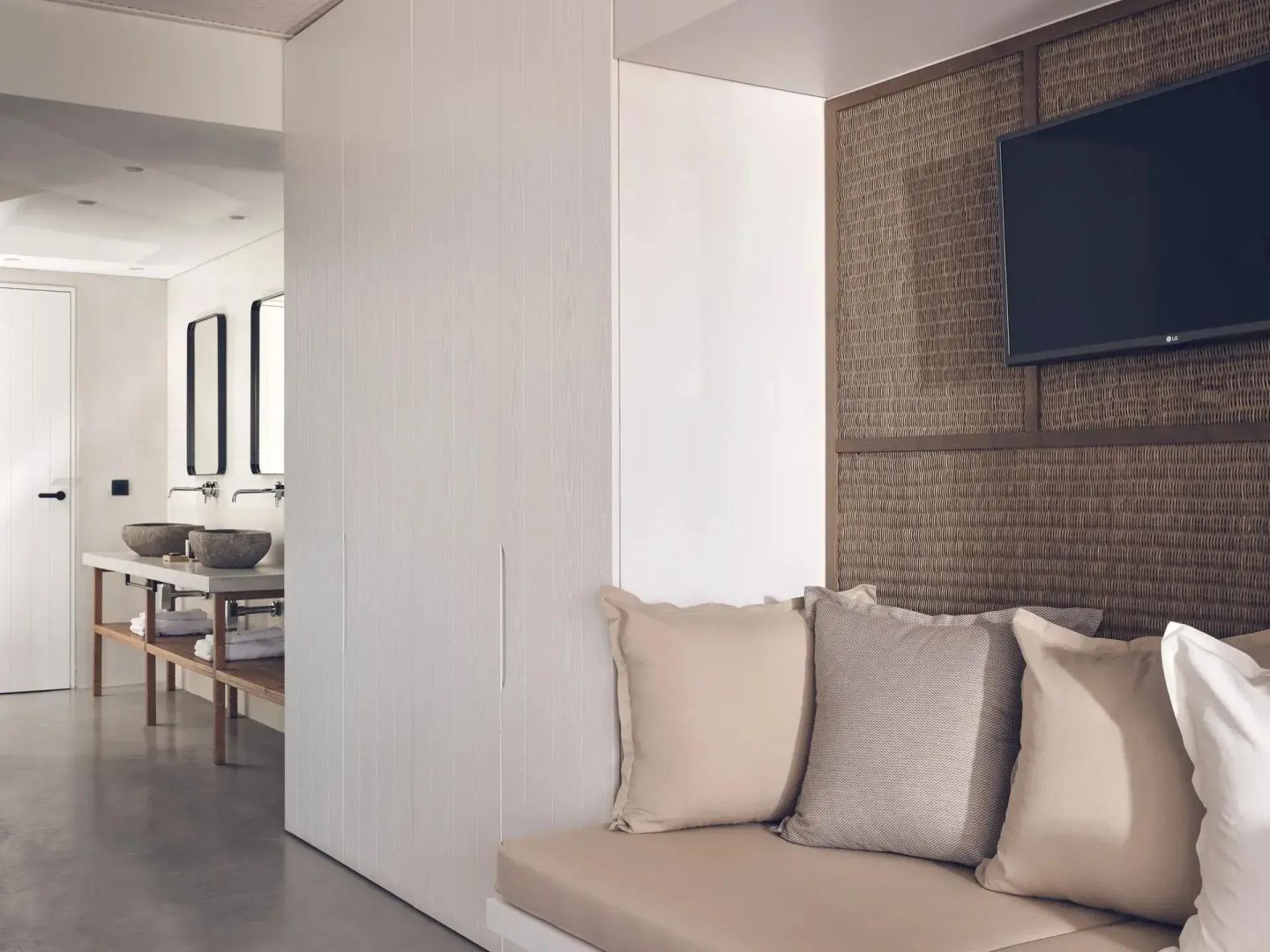 Sitznische mit beigen Kissen und Fernseher an einer geflochtenen Wand.