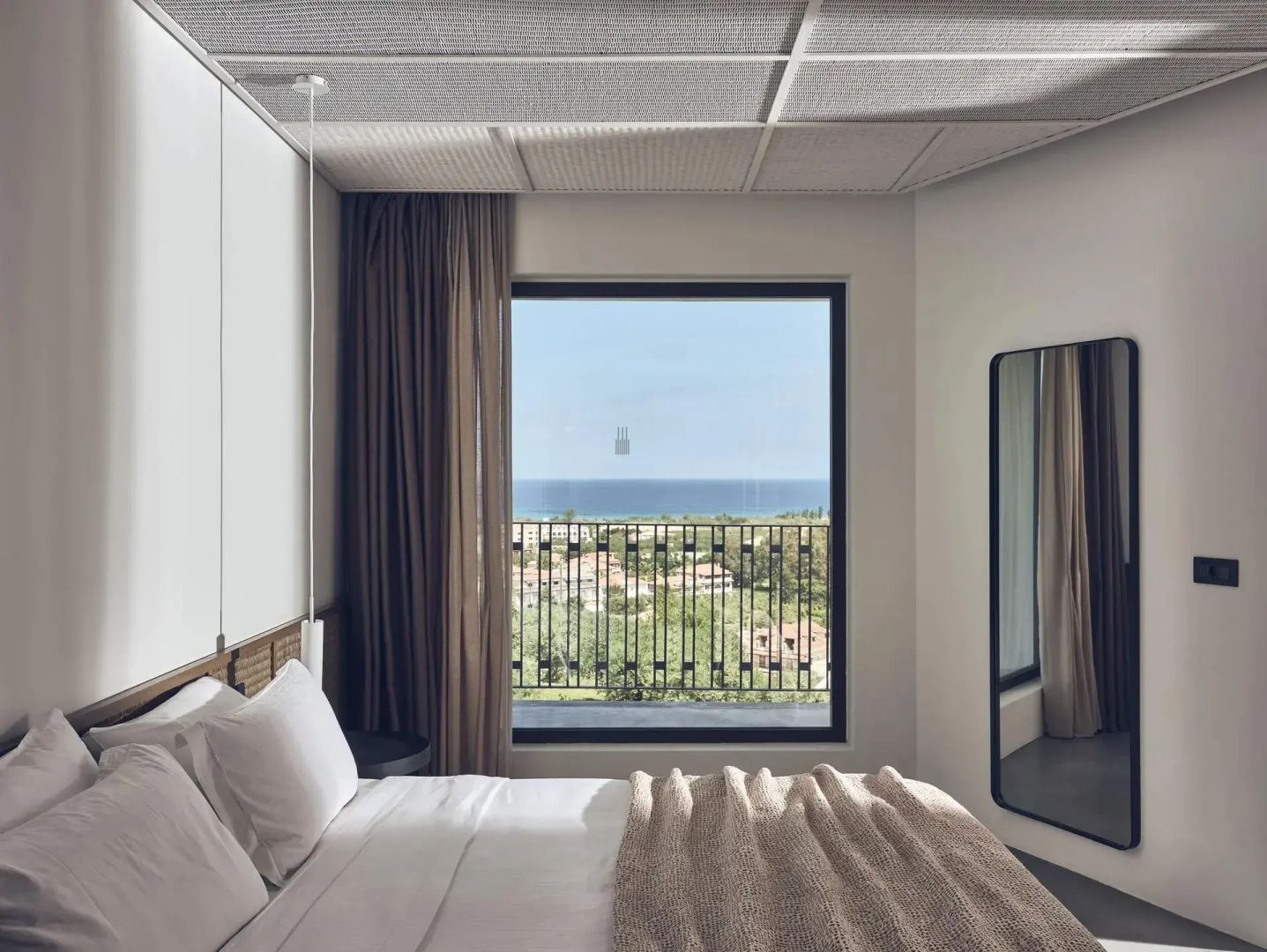 Blick aus dem Hotelzimmerfenster über grüne Landschaft auf das blaue Meer am Horizont.
