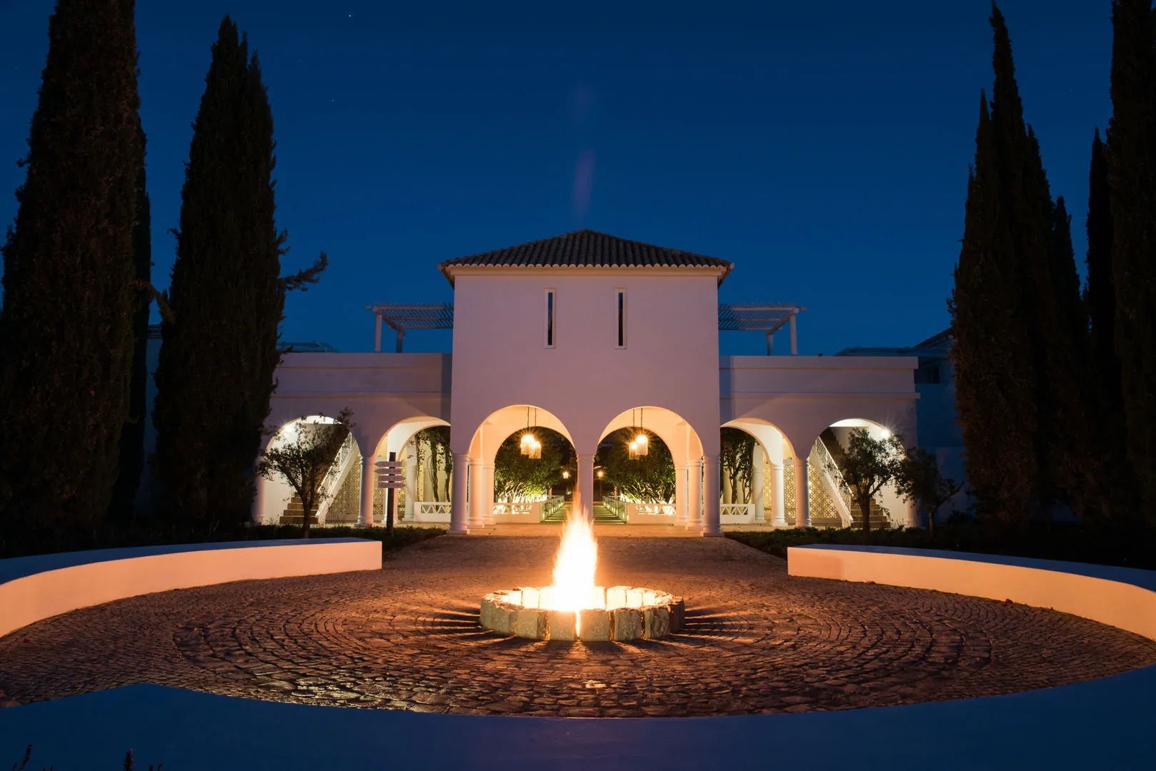 Boutique Hotel an der Algarve: das weiß getünchte Herrenhaus des Octant Vila Monte mit Zypressen und Feuerstelle in der blauen Stunde