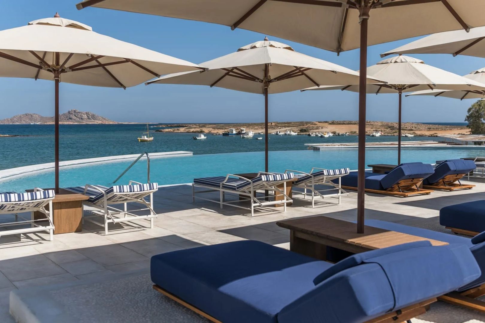 Pool mit Sonnenschirmen und Liegen mit Blick auf die Bucht und vorgelagerte Inseln im Cosme, A Luxury Collection Resort auf Paros