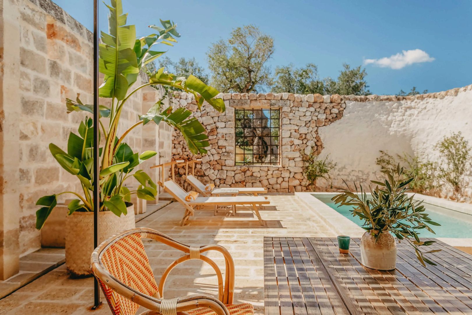 Innenhof mit Pool, Bananenstauden und Rattanmöbeln in der Masseria Calderisi bei Fasano