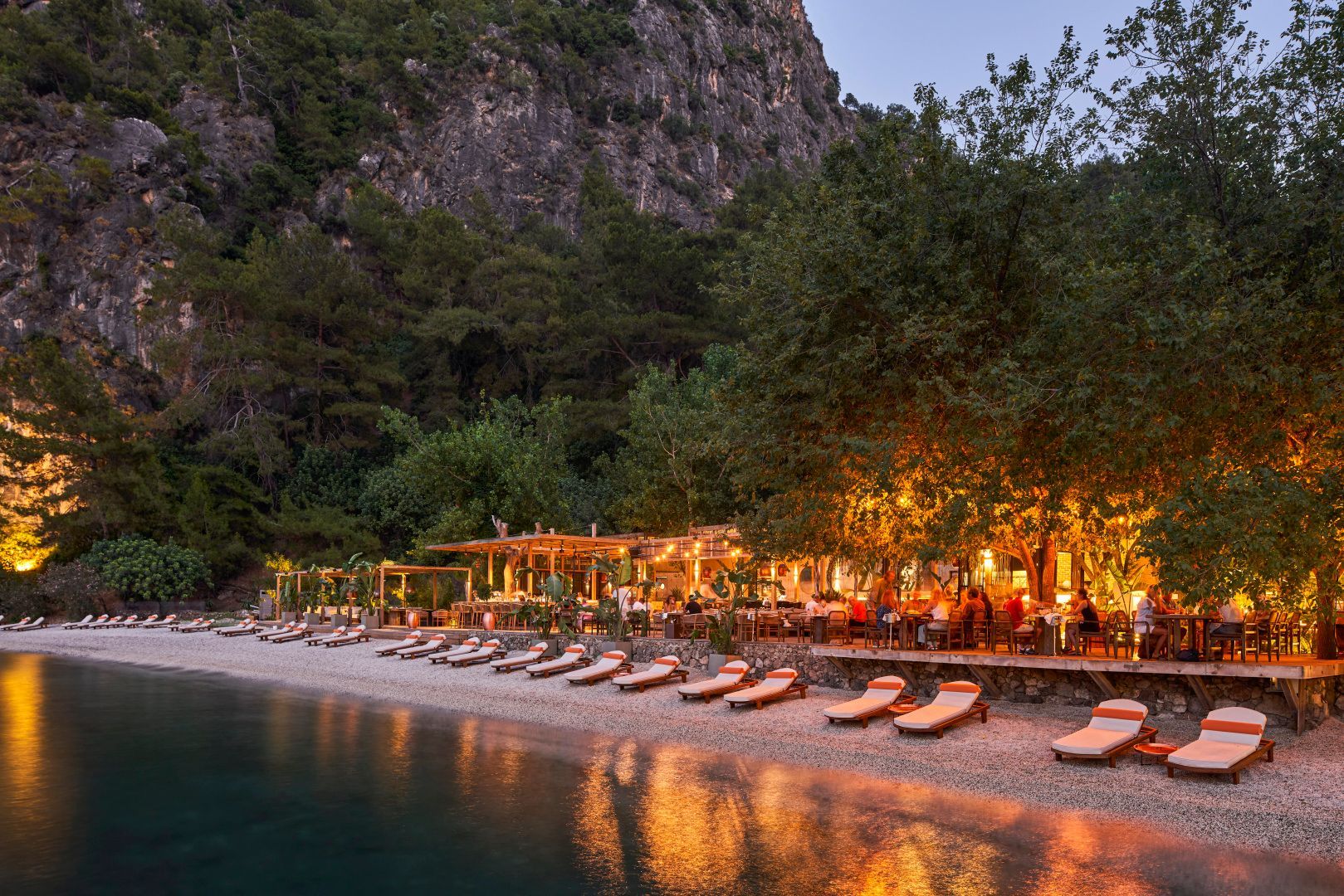 Bucht des Yazz Collective bei Fethiye am Abend mit beleuchteter Strandterrasse und Liegen