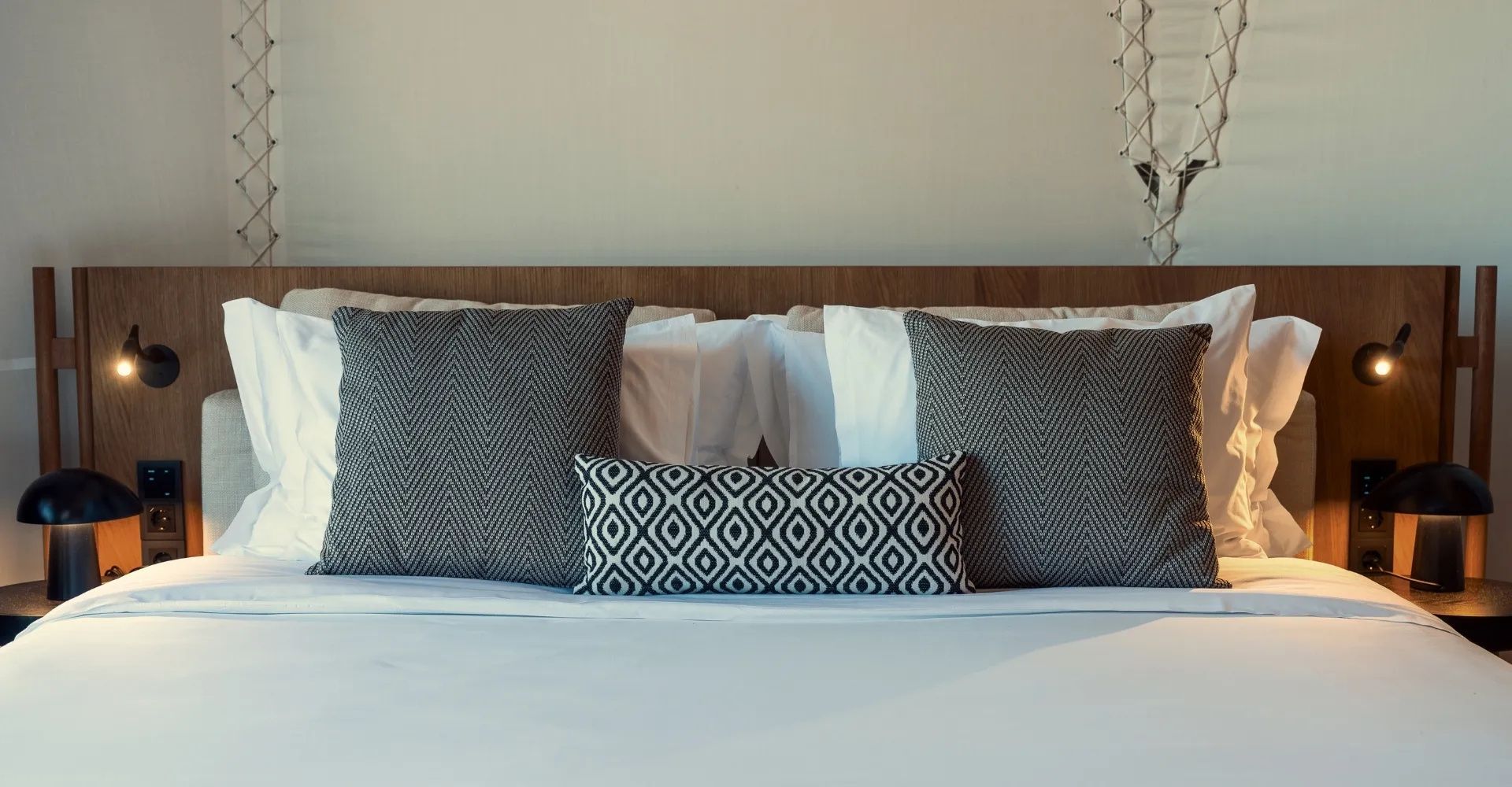Graue und gemusterte Kissen liegen auf einem weiß bezogenen Doppelbett.