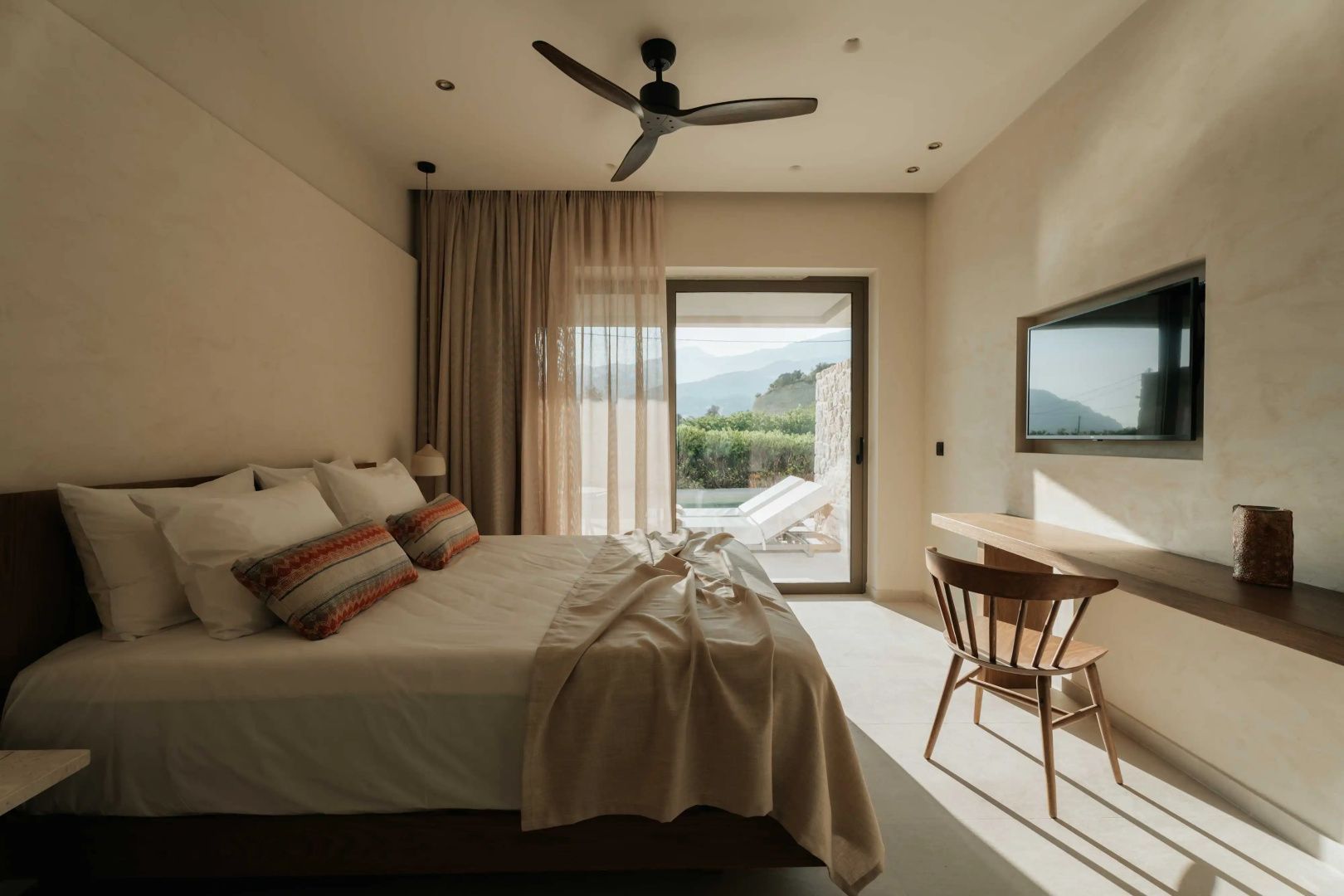 Helles Hotelzimmer mit Doppelbett, Deckenventilator, Schreibtisch und Blick auf die Terrasse.